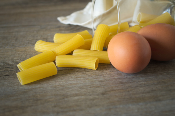 Comida italiana. Massa (rigatoni) com ovos na mesa de madeira em pouca luz
 - Foto, Imagem