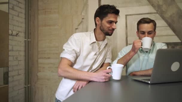 Δύο νεαροί επαγγελματίες πίνοντας καφέ να κοιτάξει στον υπολογιστή και να μιλήσει - Πλάνα, βίντεο