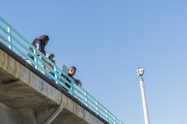 Woman and man look down from the blue railing of Manhattan Beach - Zdjęcie, obraz