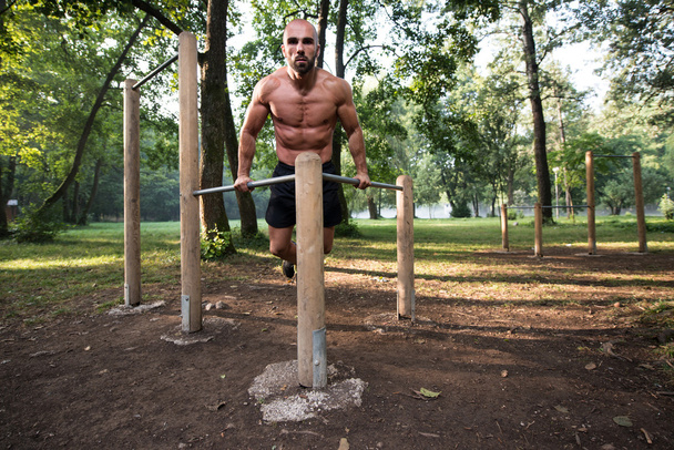 Gespierde Man Workout op Bars In Outdoor sportschool - Foto, afbeelding