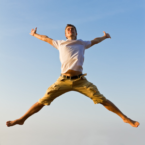 Happy young man jumping against blue sky background - Valokuva, kuva