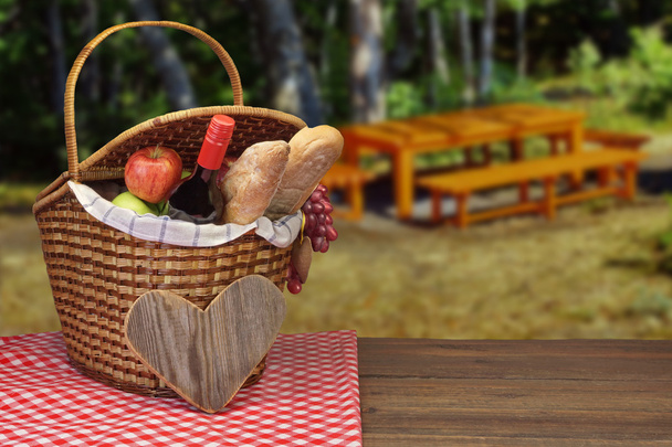 Cesta de picnic con botella de vino, pan y frutas en la mesa
 - Foto, Imagen
