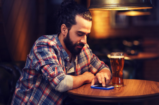 man with smartphone and beer texting at bar - 写真・画像