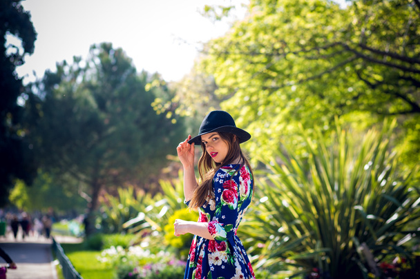 pretty slim girl with long hair in an elegant hat in a simple flowered dress walking in the summer in the park at sunset - Foto, immagini