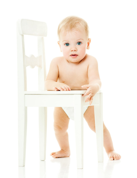 baby holds on to a white chair - Foto, Imagen
