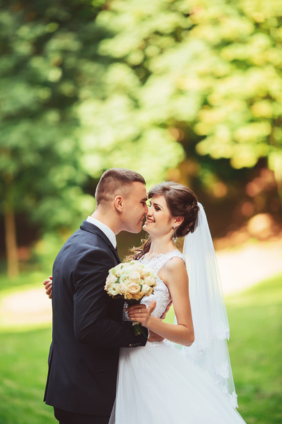 Young couple kissing in wedding gown. Bride holding bouquet of flowers - Fotografie, Obrázek