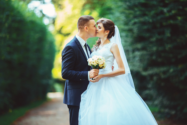 Young couple kissing in wedding gown. Bride holding bouquet of flowers - Фото, зображення