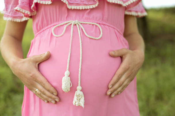 pregnant woman in pink dress, holding her tummy - Foto, imagen