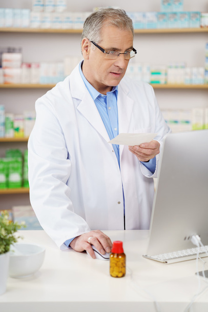 Serious pharmacist in lab coat with prescription - Фото, изображение