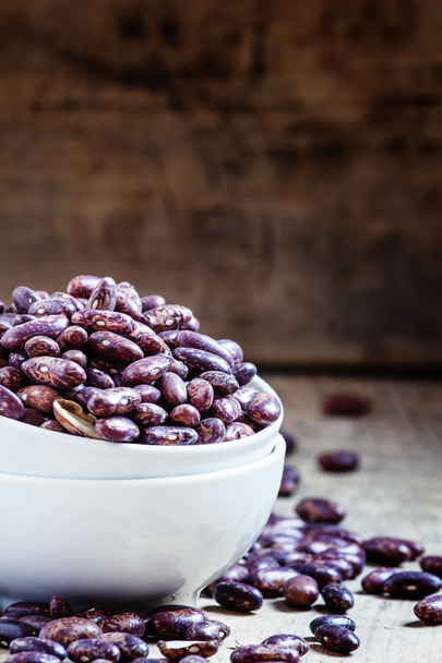 Purple-brown dry beans in a white porcelain bowl  - Fotó, kép