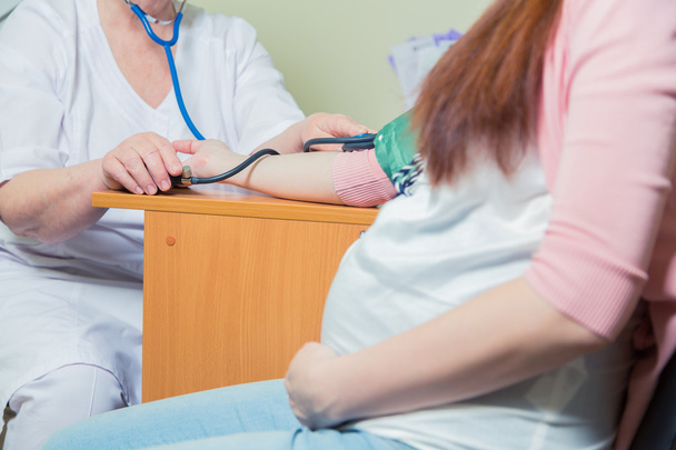 Doktor klinikte hamile bir kadının kan basıncını ölçüyor. - Fotoğraf, Görsel