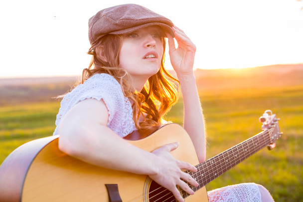 Country  girl sitting with acoustic guitar at field  - 写真・画像