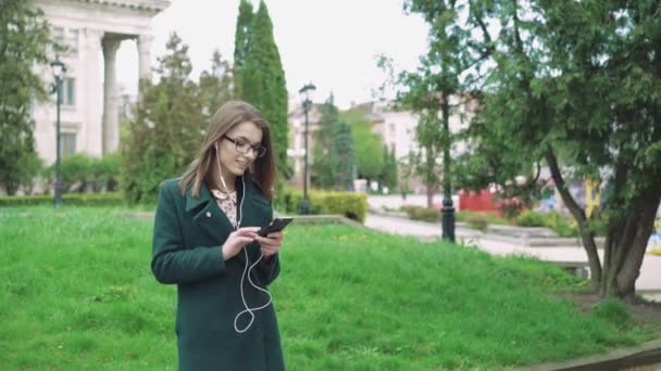 Pretty girl listening to the music win earphones outdoor 4k - Materiał filmowy, wideo