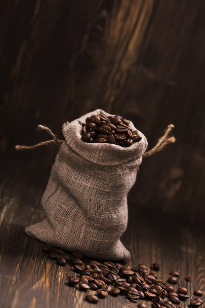Coffee beans in burlap bags over wooden background - Foto, afbeelding