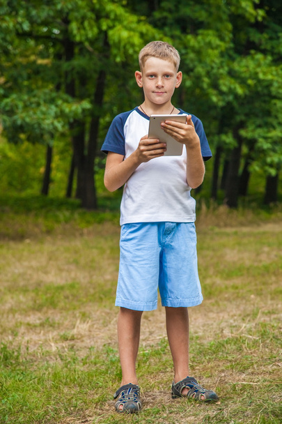 Cute young caucasian kid working with tablet in park. - Foto, Bild