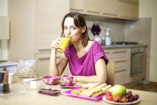 Portrait of female model drinking orange juice at home during breakfast - Фото, изображение