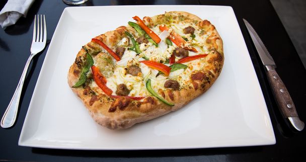 Κοντινό πλάνο σε μια φρέσκια πίτσα σε εστιατόριο με κεφτέδες, κόκκινες και πράσινες πιπεριές και τυρί μοτσαρέλα. - Φωτογραφία, εικόνα
