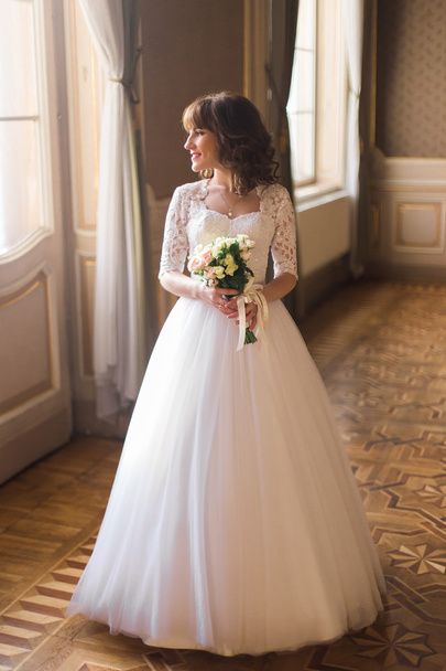 Full length view of beautiful woman posing in wedding dress near window at luxury interior - Фото, изображение