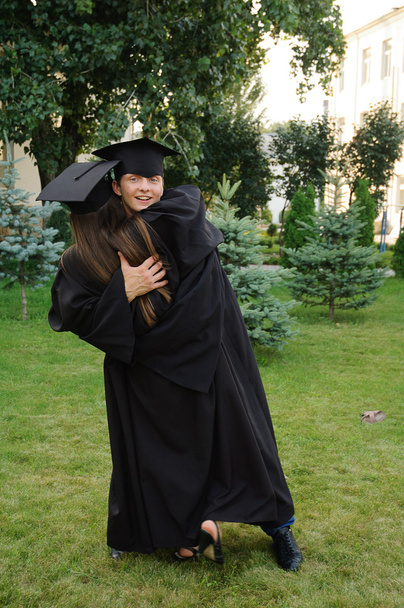 Студент в чорному одязі випускник грайливо обіймає дівчину
 - Фото, зображення