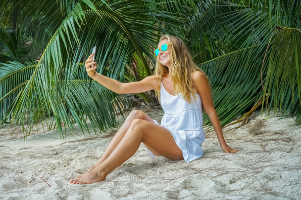 Young woman sitting on a tropical beach and photographed - Фото, зображення