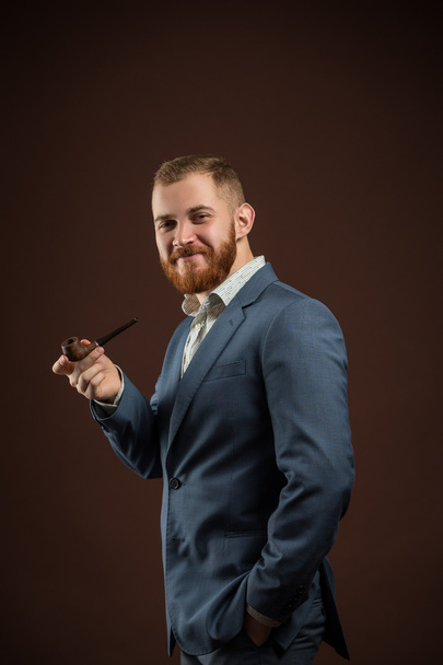 Elegant smiling man with beard holding smoking pipe - Фото, изображение