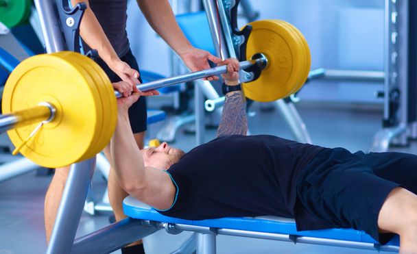 Young man lifting the barbell in gym with instructor - Photo, image