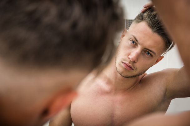 Young man looking at his hair in bathroom mirror - Fotografie, Obrázek
