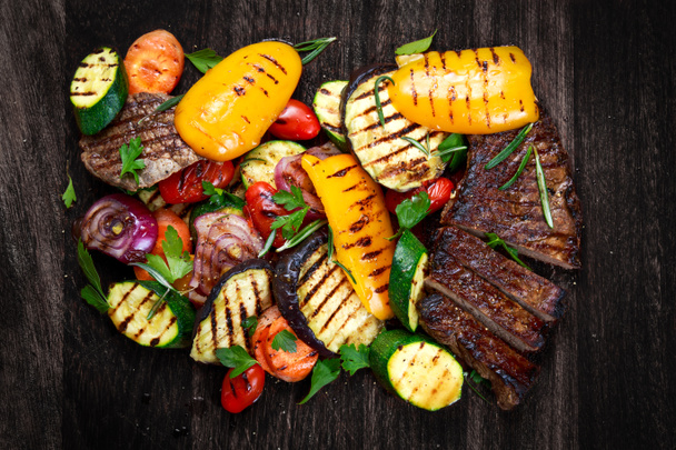 Beef steak and Grilled vegetables. On cutting dark board background - Photo, Image