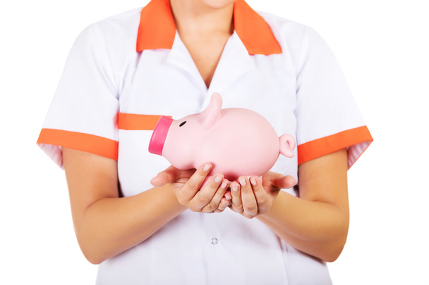 Young female doctor or nurse holding a piggybank - 写真・画像