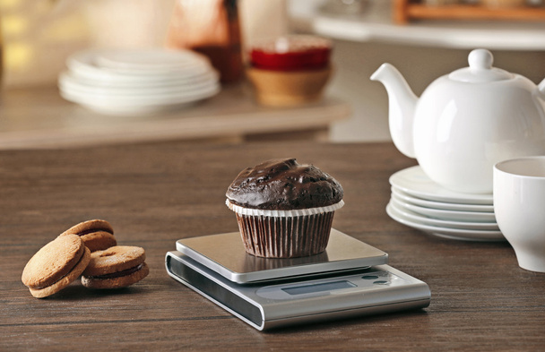 Chocolate cupcake and digital kitchen scales on wooden table - Foto, afbeelding