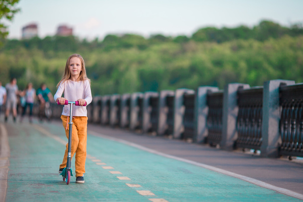 Чарівна маленька дівчинка їде на скутері в літньому парку
 - Фото, зображення