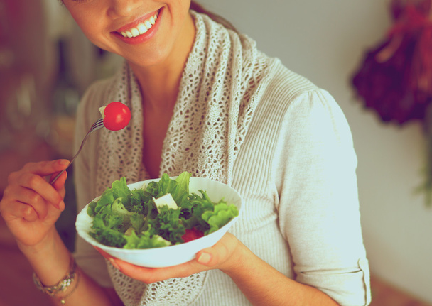 若いです女性食べる新鮮なサラダで現代的なキッチン - 写真・画像