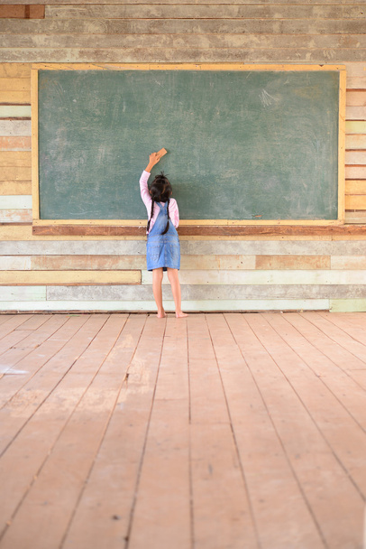 Kid earasing on the old green chalkboard; Wood floor - Foto, Imagen