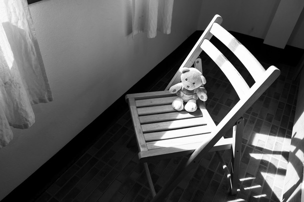 Mignon ours en peluche assis seul sur la chaise près de la fenêtre, noir et blanc
 - Photo, image