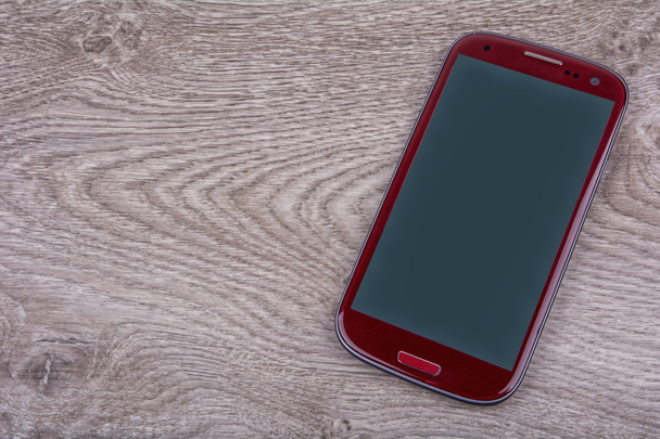 Teléfono móvil rojo sobre fondo de madera
 - Foto, imagen