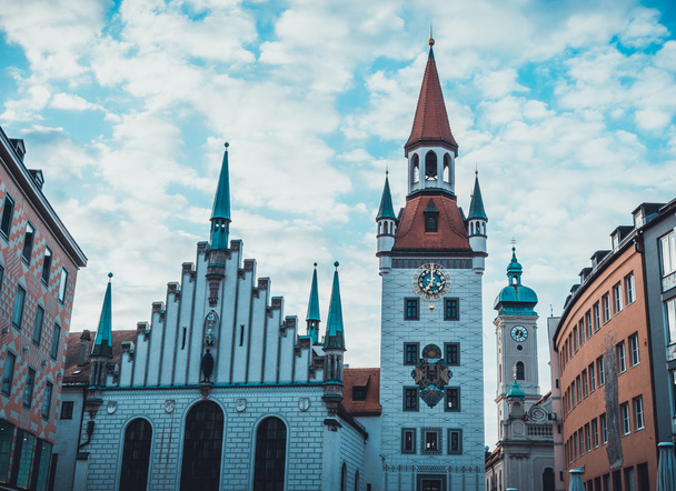 Ratusz w Marienplatz, Monachium, Niemcy z charakterystyczną gotycką fasadą przeciwko zachmurzonemu błękitnemu niebu w widoku z niskiego kąta - Zdjęcie, obraz
