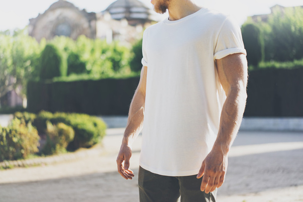 Picture Bearded Muscular Man Wearing White Blank t-shirt. Green City Garden Background at sunset. Horizontal Mockup - Photo, image