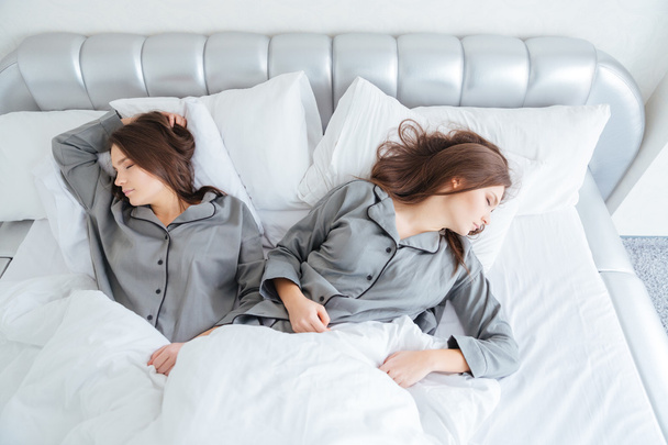 Two attractive young sisters twins sleeping in bed - Photo, Image