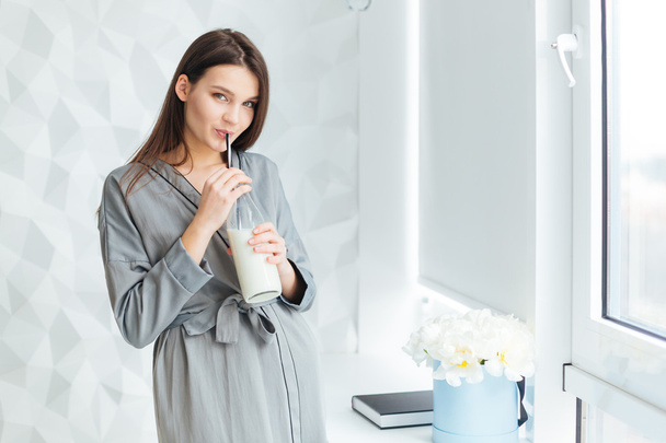Charming woman in bathrobe drinking milk fom bottle with straw  - Фото, изображение