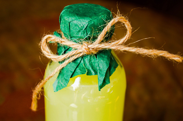 παραδοσιακά ιταλικά ηδύποτο που παράγεται από τα λεμόνια limoncello σε ένα μικρό μπουκάλι σε ένα όμορφα περιτυλιγμένο λαιμό, σε ένα παλιό αγροτικό σκούρο φόντο - Φωτογραφία, εικόνα
