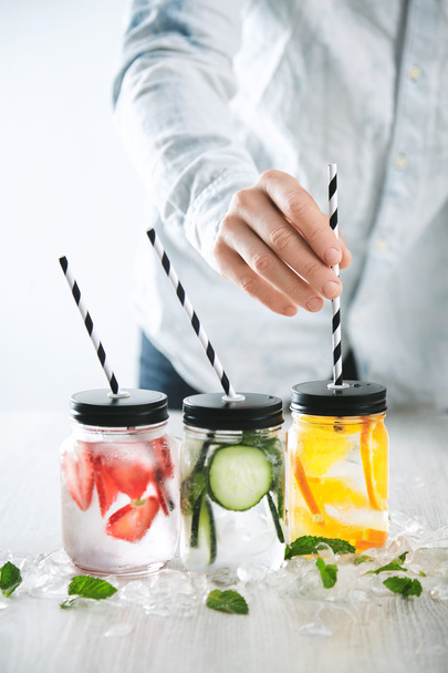 Bartender puts striped drinking straws  in jars with lemonades - Fotó, kép