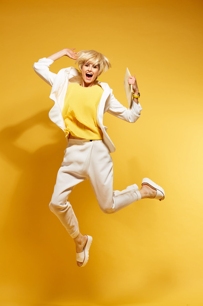 Young girl having fun and jumping. Smiling girl with yellow background wearing fashion clothes - Foto, Imagem