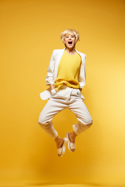 Young girl having fun and jumping. Smiling girl with yellow background wearing fashion clothes - Fotografie, Obrázek