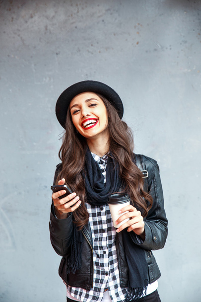 Young pretty girl in hat using smartphone to make a call in the street. - Foto, imagen