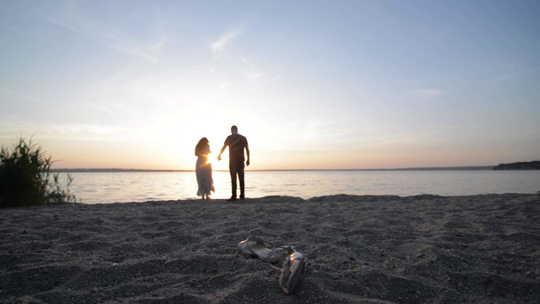 Paar erwartet Baby beim Spazierengehen am Flussufer und hält Händchen bei Sonnenuntergang - Filmmaterial, Video
