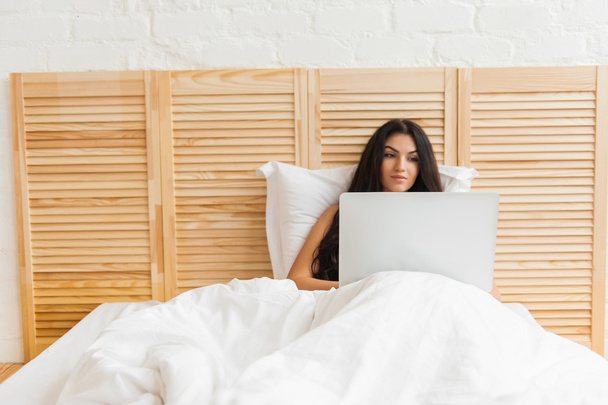 Smiling woman lying on bed with laptop in the morning - Фото, изображение