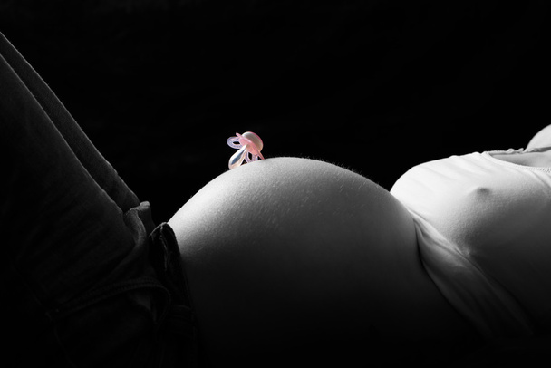 llave de color del chupete en el vientre de la madre embarazada en el fondo negro
 - Foto, Imagen