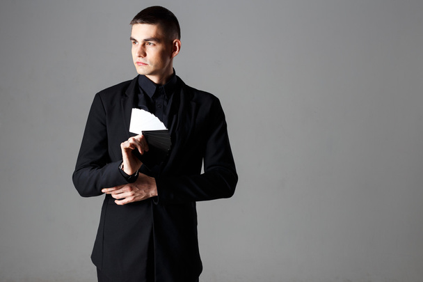 Portrait of handsome man magician in a black suit holding cards in a hand - Foto, afbeelding