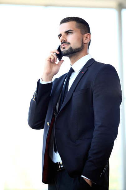Young businessman standing in office lobby, using smartphone - Foto, Imagen