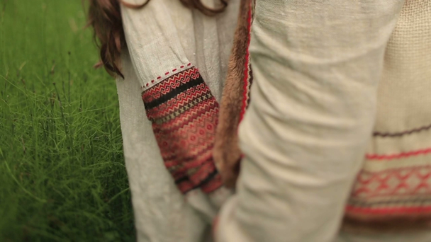 Красива дівчина брюнетка в традиційній українській сорочці з квіткою вінок цілує свого хлопця на зеленому полі весни - Кадри, відео